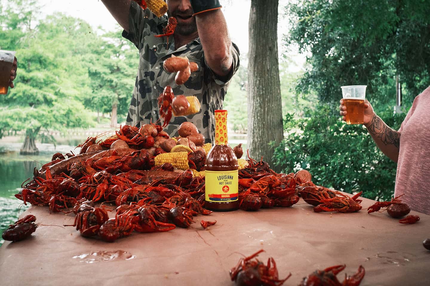 Person pouring out crawdads with a bottle of Louisiana Hot Sauce